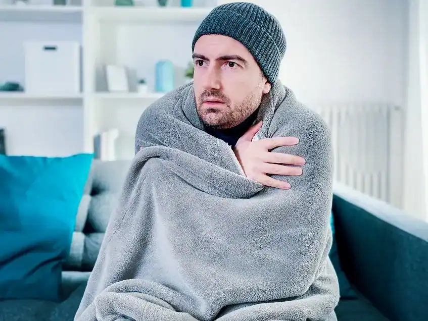 Mann sitzt in eine Decke gewickelt in der kalten Wohnung